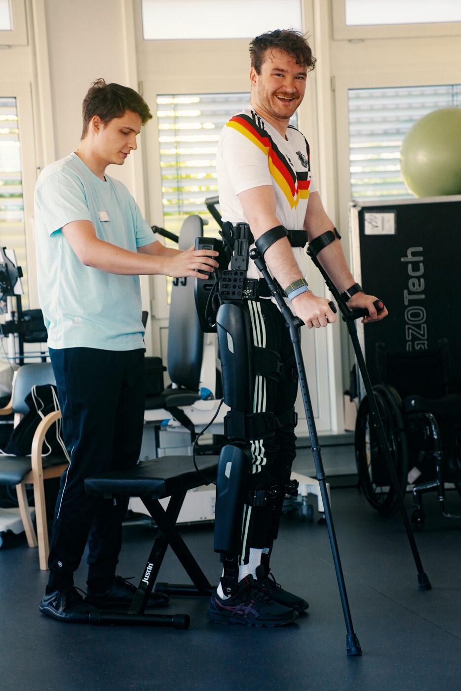 Therapeut begleitet einen Patienten beim Gangtraining mit robotischem Exoskelett und Unterarmgehstützen